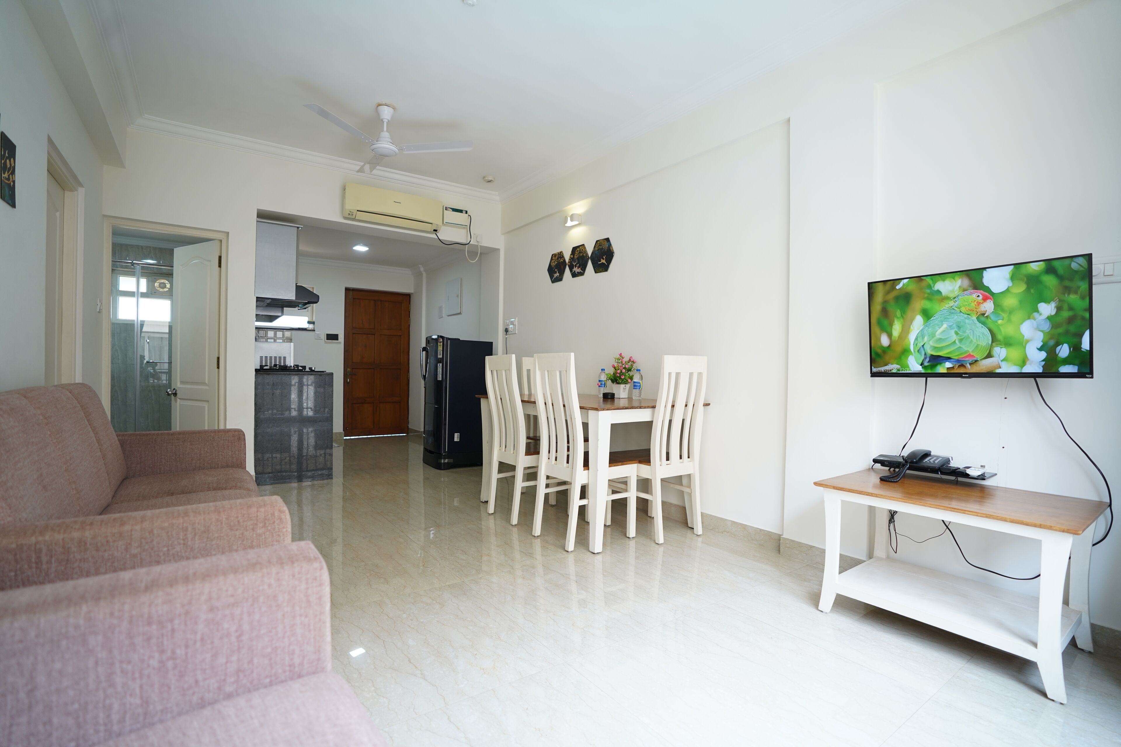 Ein Wohnzimmer mit einer Couch, einem Essbereich mit Tisch und Stühlen, einem an der Wand montierten Fernseher und einem Deckenventilator.