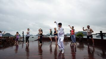 A group of people performing a dance routine on a wooden deck with a view of a body of water and mountains in the background.