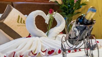 A table with a white towel arranged in a heart shape, a rose, and a champagne bottle in a glass holder.