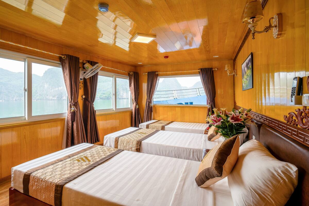 A cabin with two beds, wooden walls, a window with curtains, a ceiling fan, and a view of a body of water.