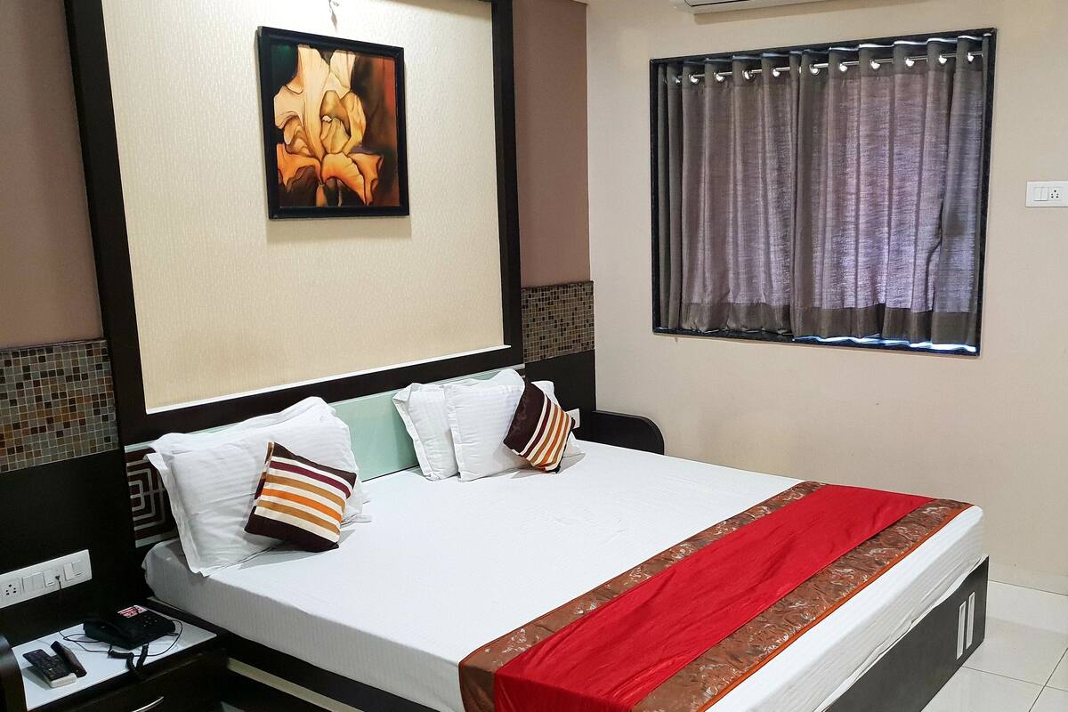 A neatly made bed with a red and brown bedspread, white pillows, and a framed picture on the wall above.