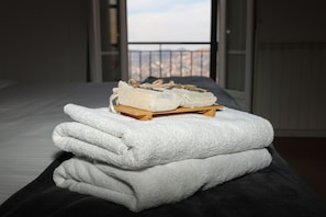 A bed with a view of a balcony and a wooden stool with a woven bag and folded towels.