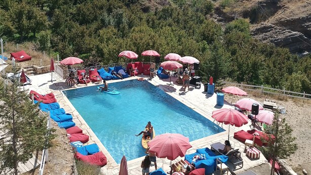 Zona de piscina con sillas reclinables azules y rojas, sombrillas y vistas despejadas de las colinas circundantes.