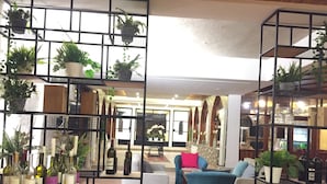 Un amplio salón con diseño moderno, que cuenta con una gran zona de estar con sofás y una mesa de centro, rodeado de estanterías con plantas en macetas y botellas de vino.