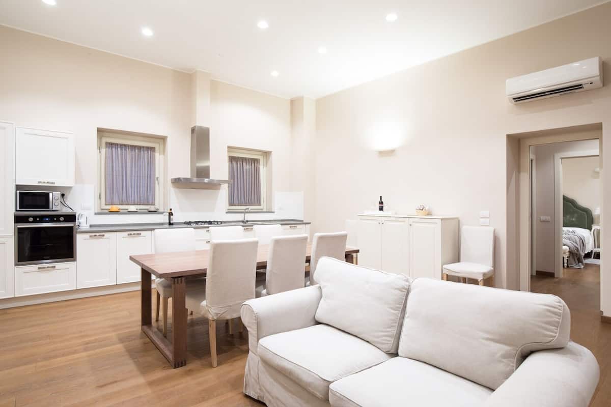 Une cuisine moderne avec des meubles blancs, une table à manger avec des chaises et un canapé blanc dans une pièce lumineuse dotée d’un plancher en bois.