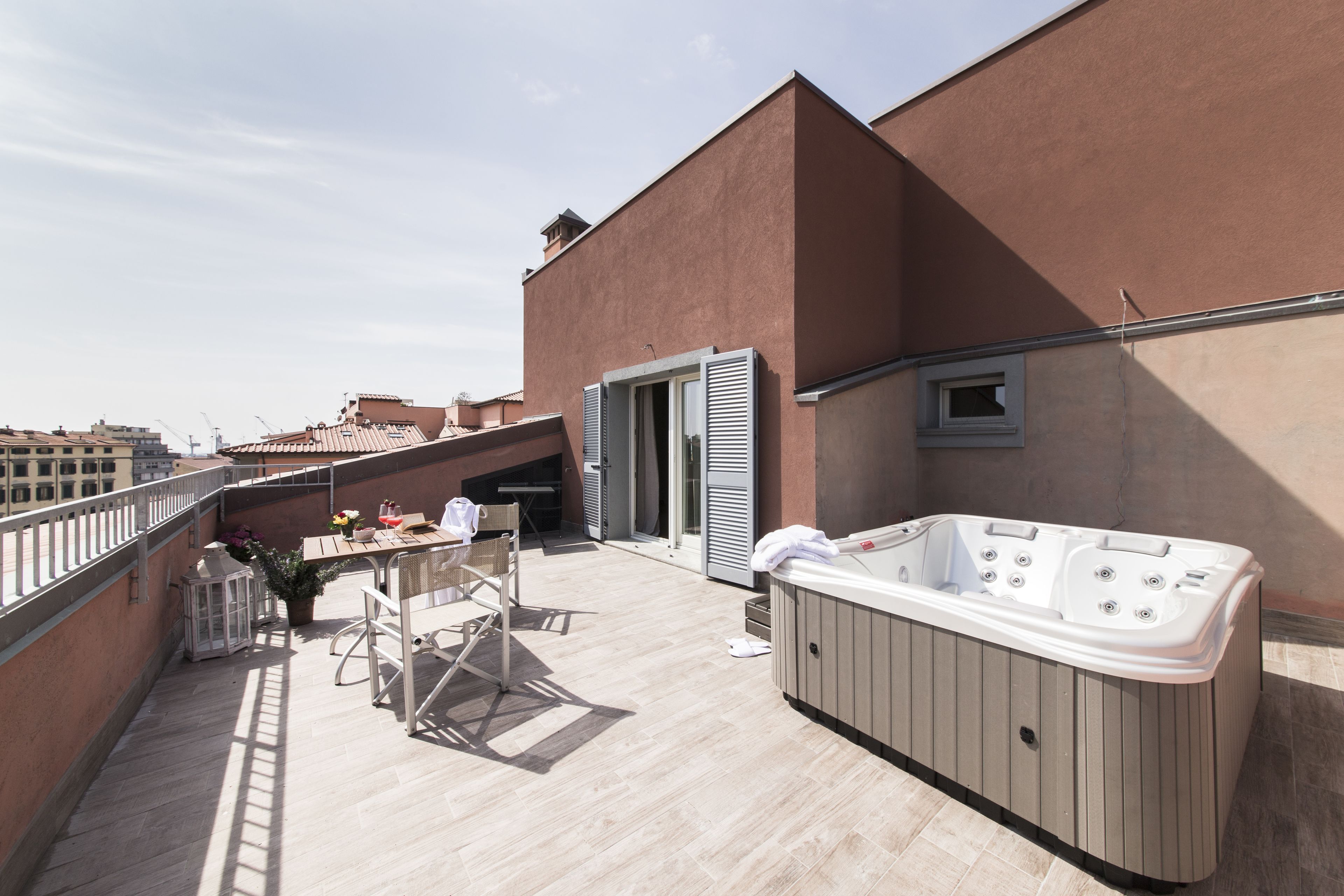 Una terraza en la azotea con un jacuzzi, una mesa con sillas y una planta en maceta.