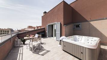 Una terraza en la azotea con un jacuzzi, una mesa con sillas y una planta en maceta.