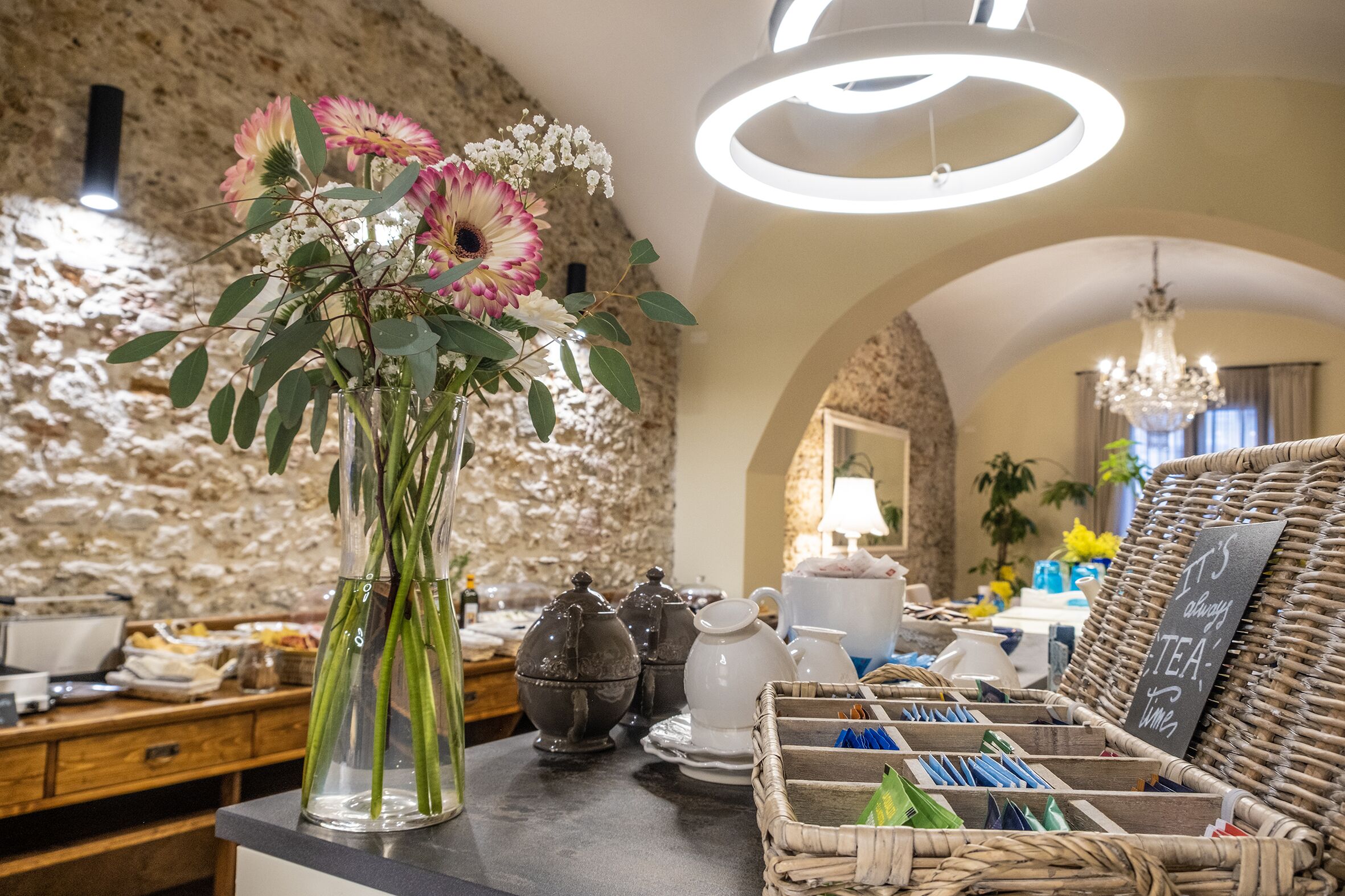 Habitació ben il·luminada amb paret de pedra, un ram de flors, servei de te i una cistella de vimet amb bossa de te.