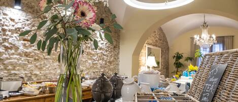 Habitació ben il·luminada amb paret de pedra, un ram de flors, servei de te i una cistella de vimet amb bossa de te.