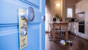 Una puerta con un cartel que dice "CANE IN CAMERA", una mesa de comedor de madera y una cocina con armarios y electrodomésticos.