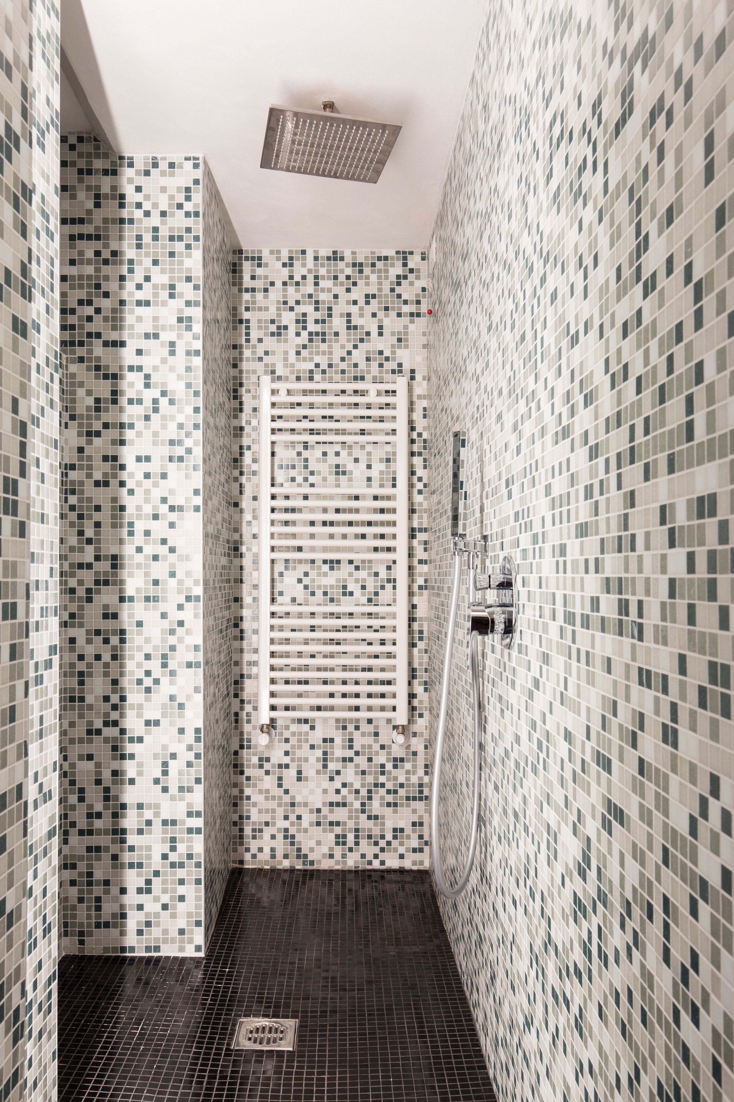 Un baño estrecho con azulejos, zona de ducha, desagüe e iluminación en el techo.