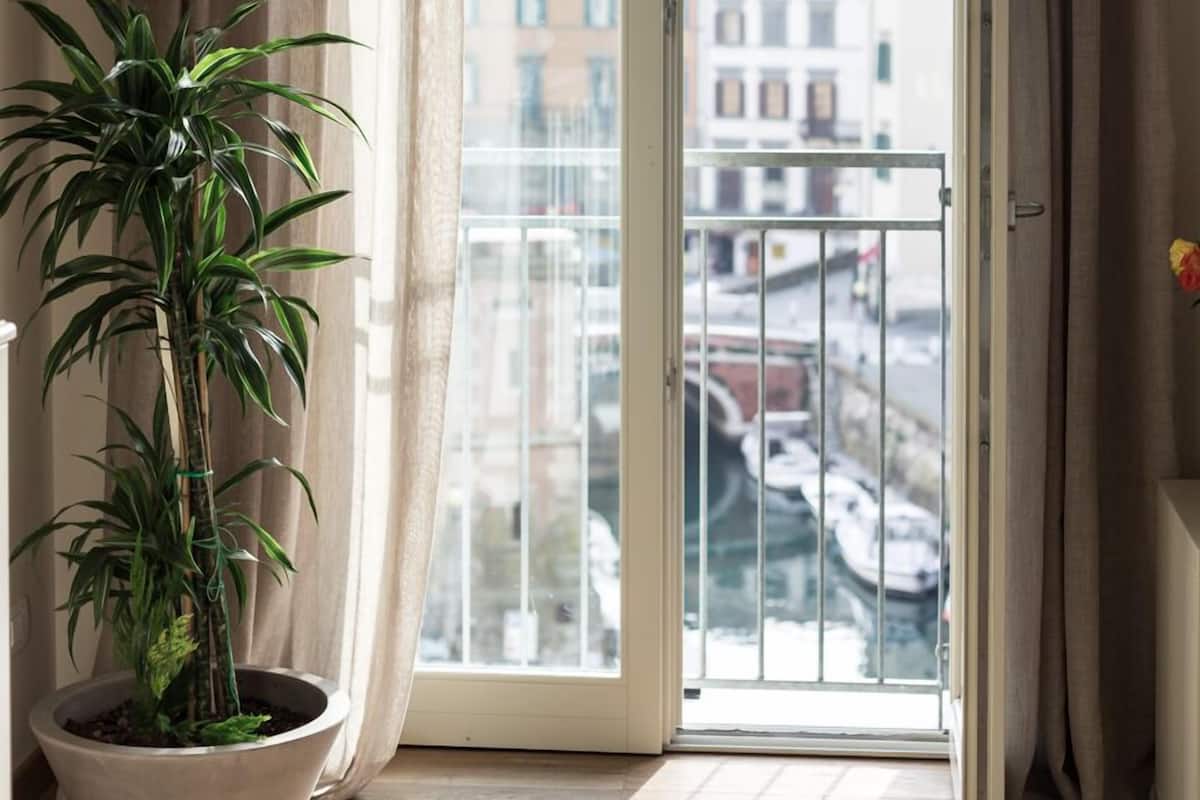 Une pièce dotée d’une grande porte-fenêtre coulissante qui donne sur un balcon offrant une vue sur les immeubles et les bateaux. Un pot de fleurs est posé sur le sol.