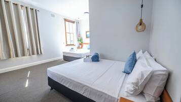 Una cama bien hecha con sábanas blancas y almohadas azules, una mesita de noche de madera y una lámpara colgante.