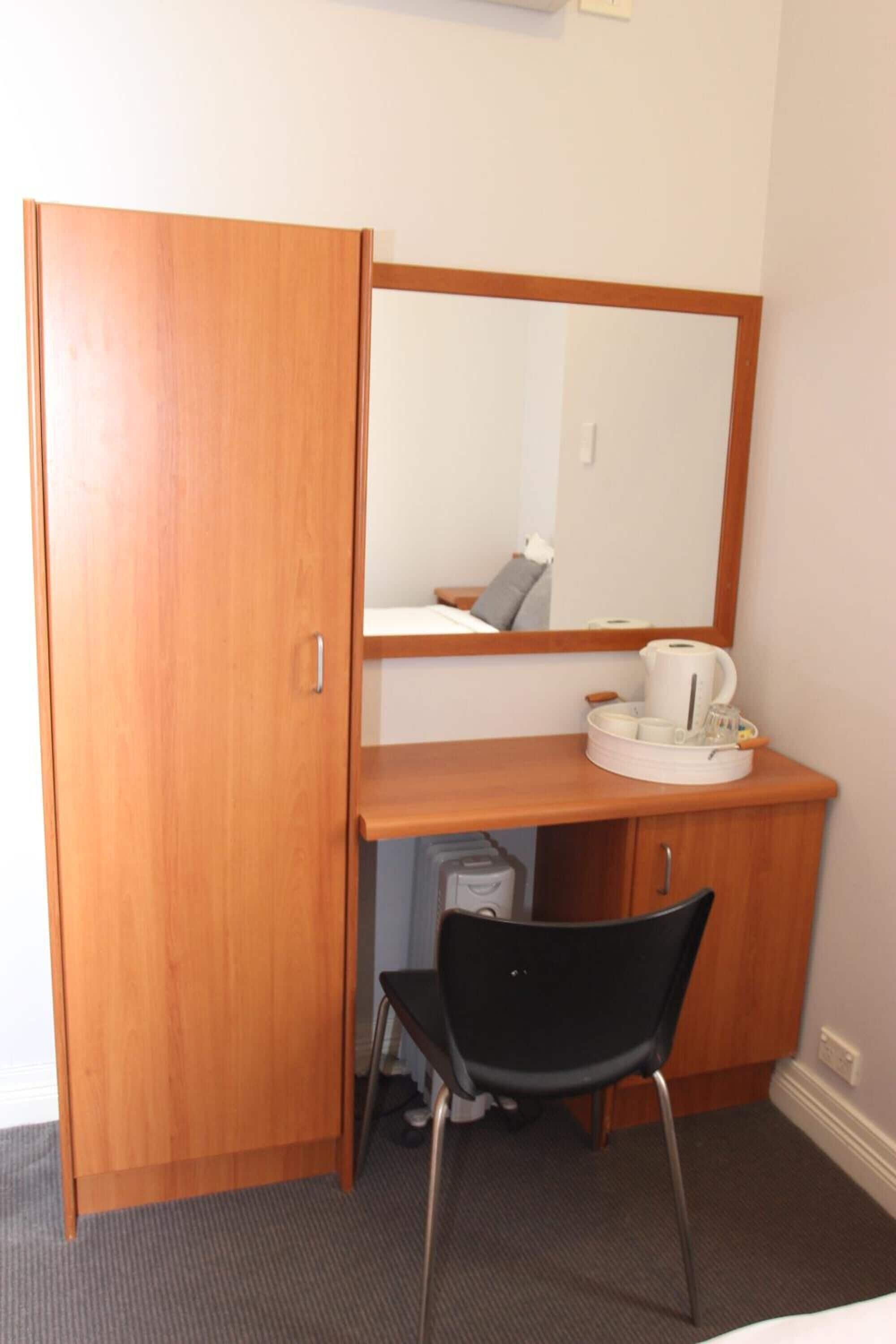 Habitación de hotel compacta con armario de madera, un escritorio pequeño con espejo, una silla y una cama.