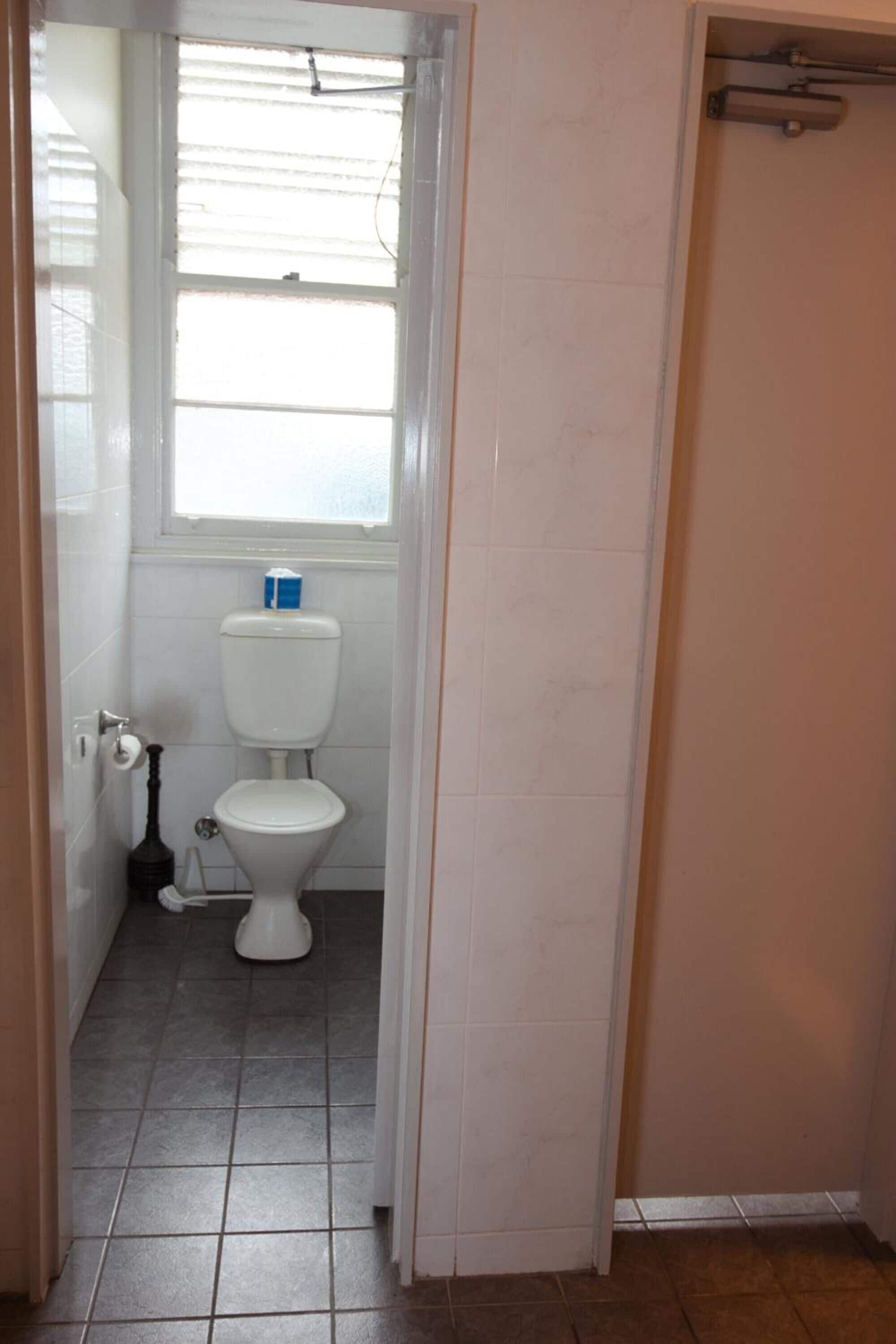 A bathroom with a toilet, a window, and a shower area.