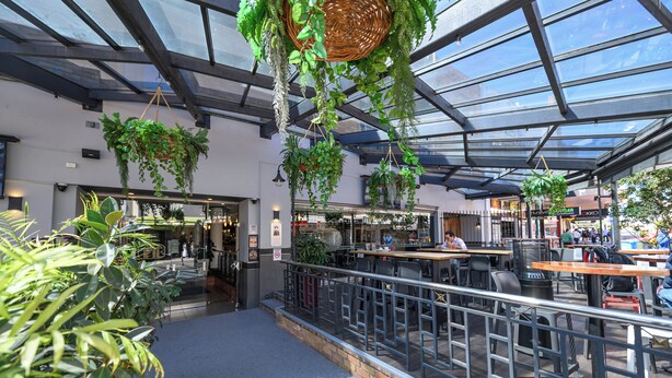 Un comedor interior con plantas colgantes, techo de cristal y asientos al aire libre.