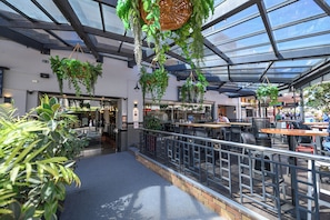 An indoor dining area with hanging plants, a glass ceiling, and outdoor seating.