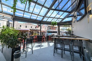 An indoor dining area with a glass ceiling, tables, chairs, and hanging plants.