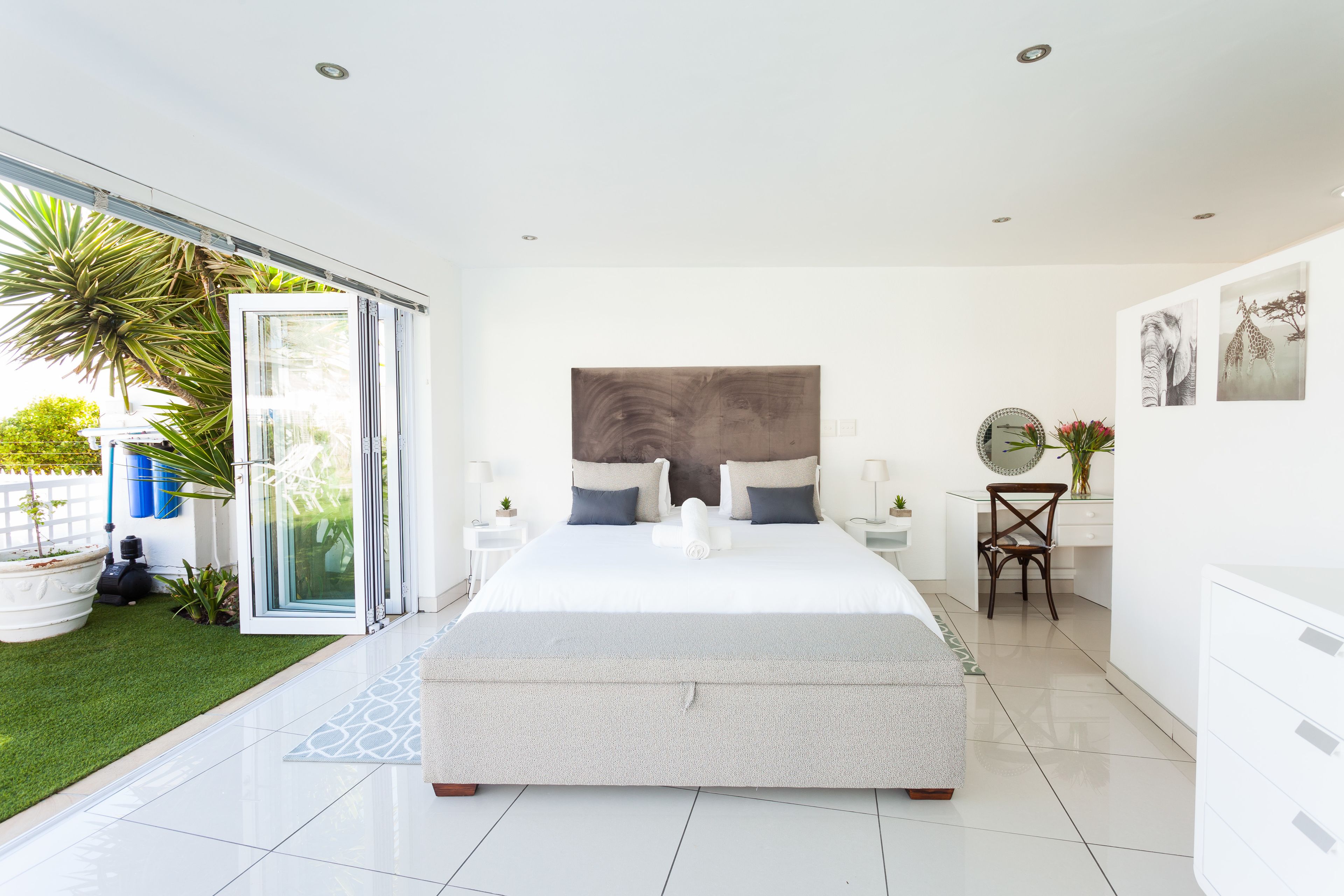 A modern bedroom with a large bed, a glass door leading to a garden, and a small desk area.