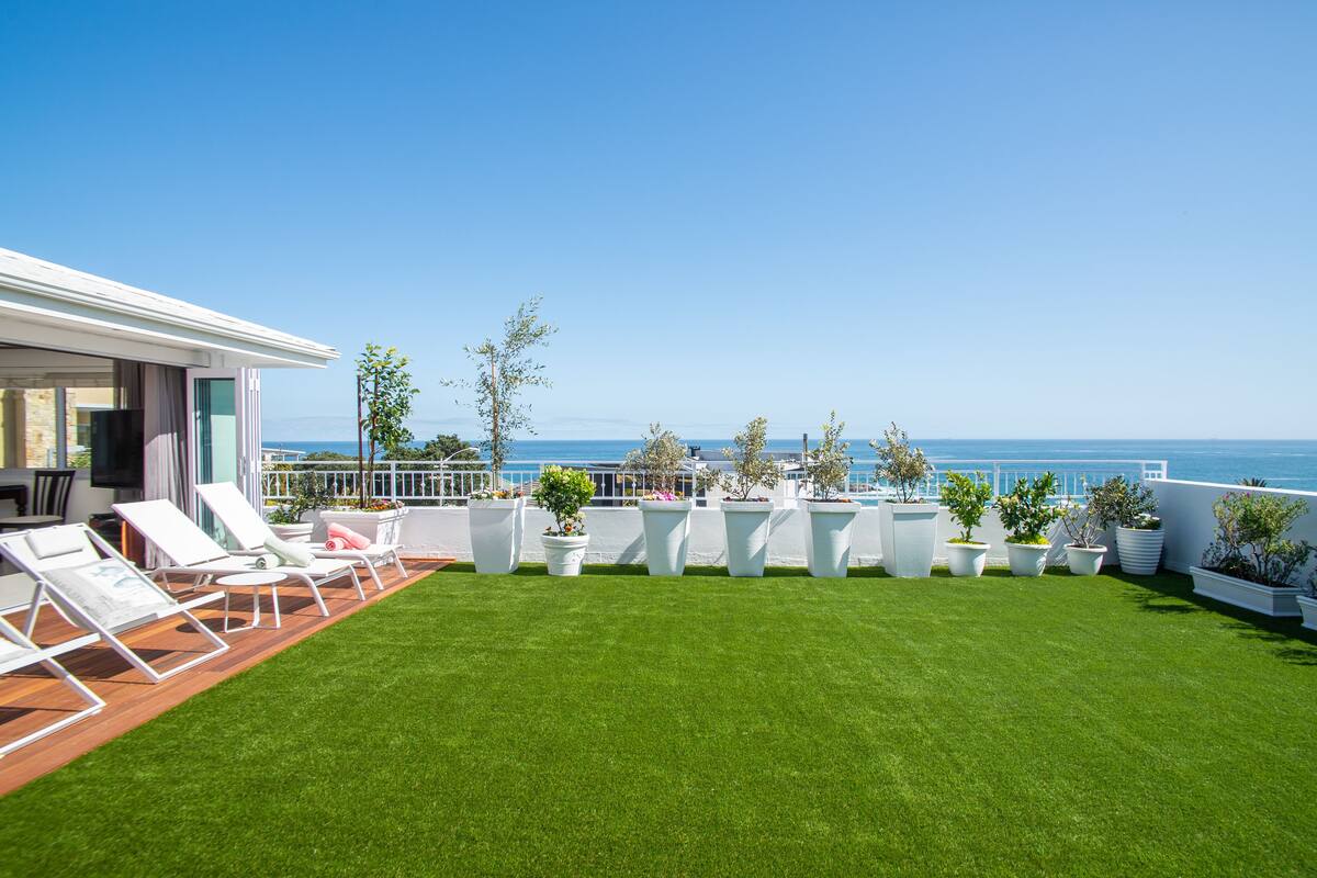 A rooftop terrace with a clear view of the ocean, a grassy lawn, and white lounge chairs.