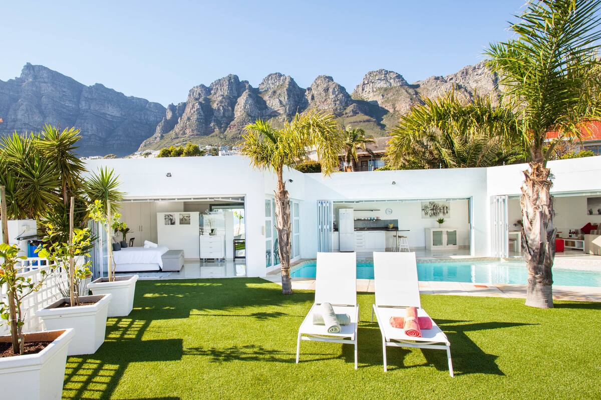 A modern house with a pool, white furniture, and a view of mountains.