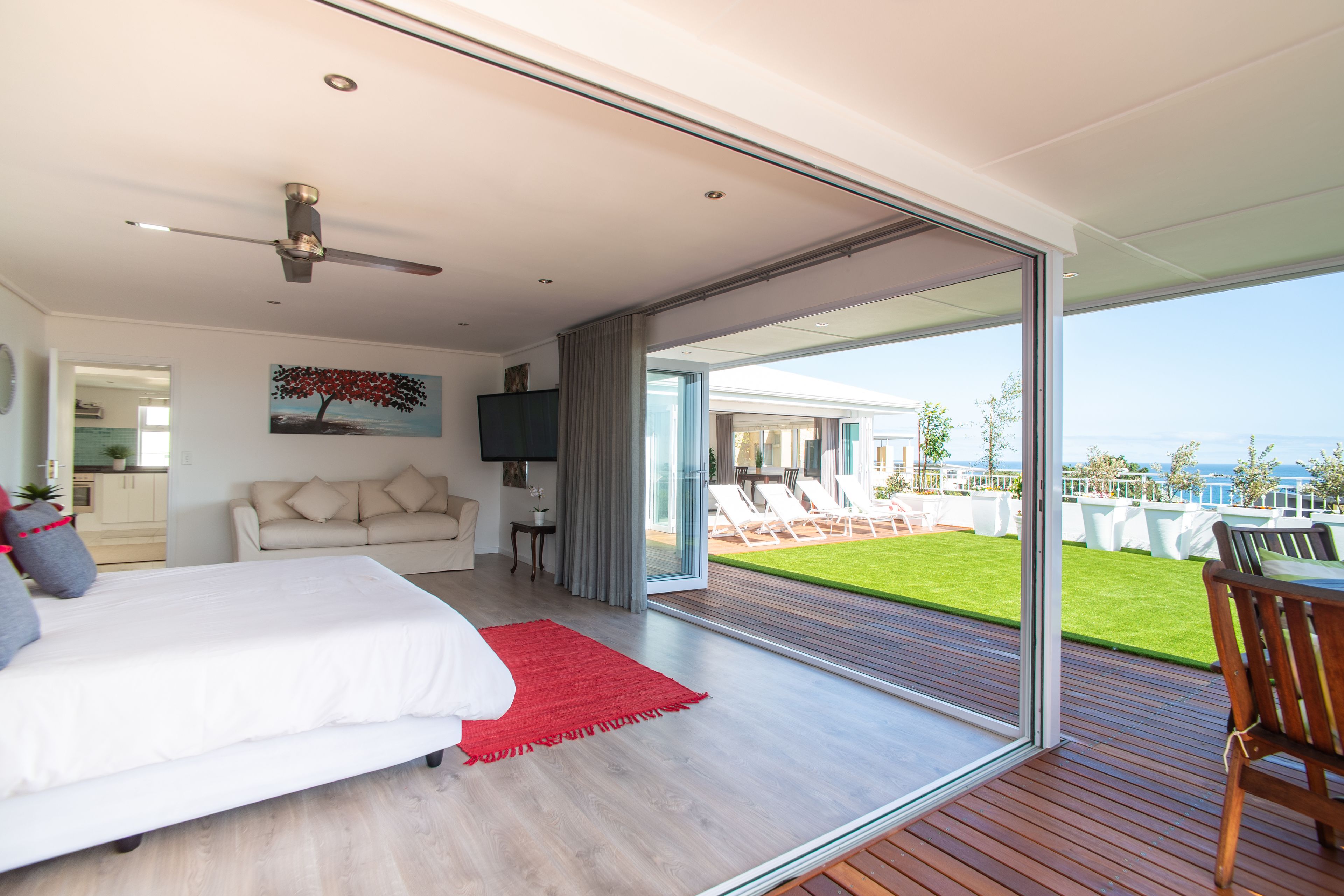 A modern bedroom with a large bed, a TV, and a view of a deck and outdoor area.