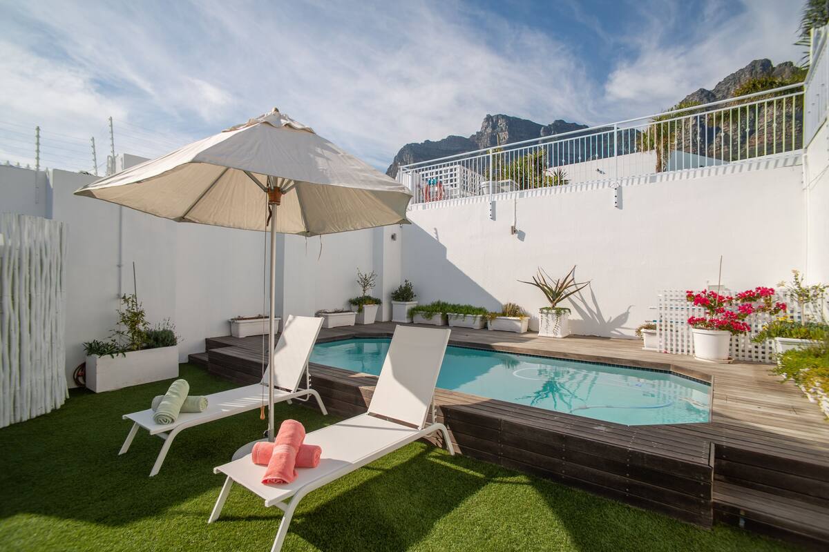 A pool area with two lounge chairs, a large umbrella, and a wooden deck.