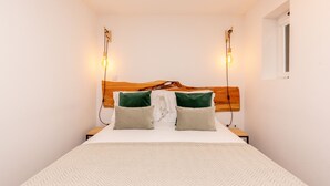 Een net opgemaakt bed met een houten hoofdbord, twee nachtkastjes en twee wandlampen.