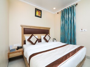 A neatly made bed with a wooden headboard, a bedside table with a phone and a book, and a wall-mounted light fixture. - OYO 15567 Hotel India International Sitare (New Delhi)