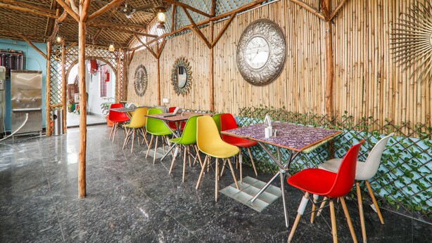 A restaurant with bamboo walls, colorful chairs, and a large clock on the wall. - OYO 15567 Hotel India International Sitare (New Delhi)