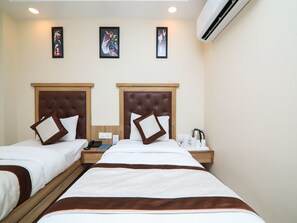 A hotel room with two beds, each with a wooden headboard, white bedding, and brown pillows. There are framed artworks on the wall, a bedside table with a phone and a kettle, and an air conditioning unit on the wall. - OYO 15567 Hotel India International Sitare (New Delhi)