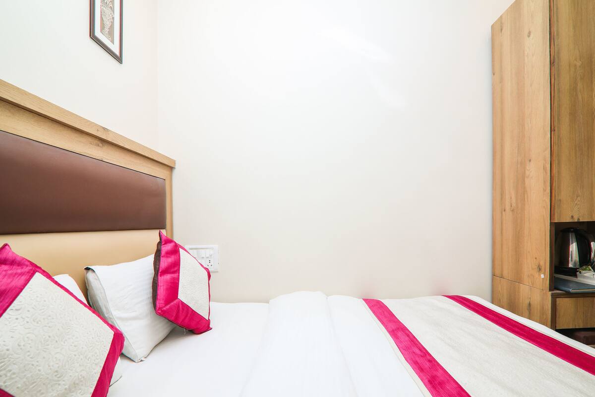 A neatly made bed with white and pink bedding, a wooden headboard, and a wooden wardrobe in a hotel room.