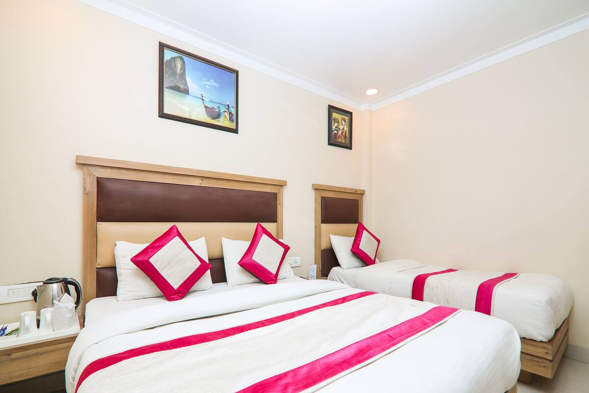 A hotel room with two beds, each with white bedding and red accents, a wooden headboard, and a painting of a beach scene above the beds.