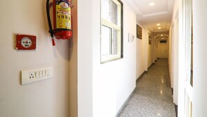 A hallway with a fire extinguisher mounted on the wall, a smoke detector, and a window with a decorative grille. - OYO 15567 Hotel India International Sitare (New Delhi)