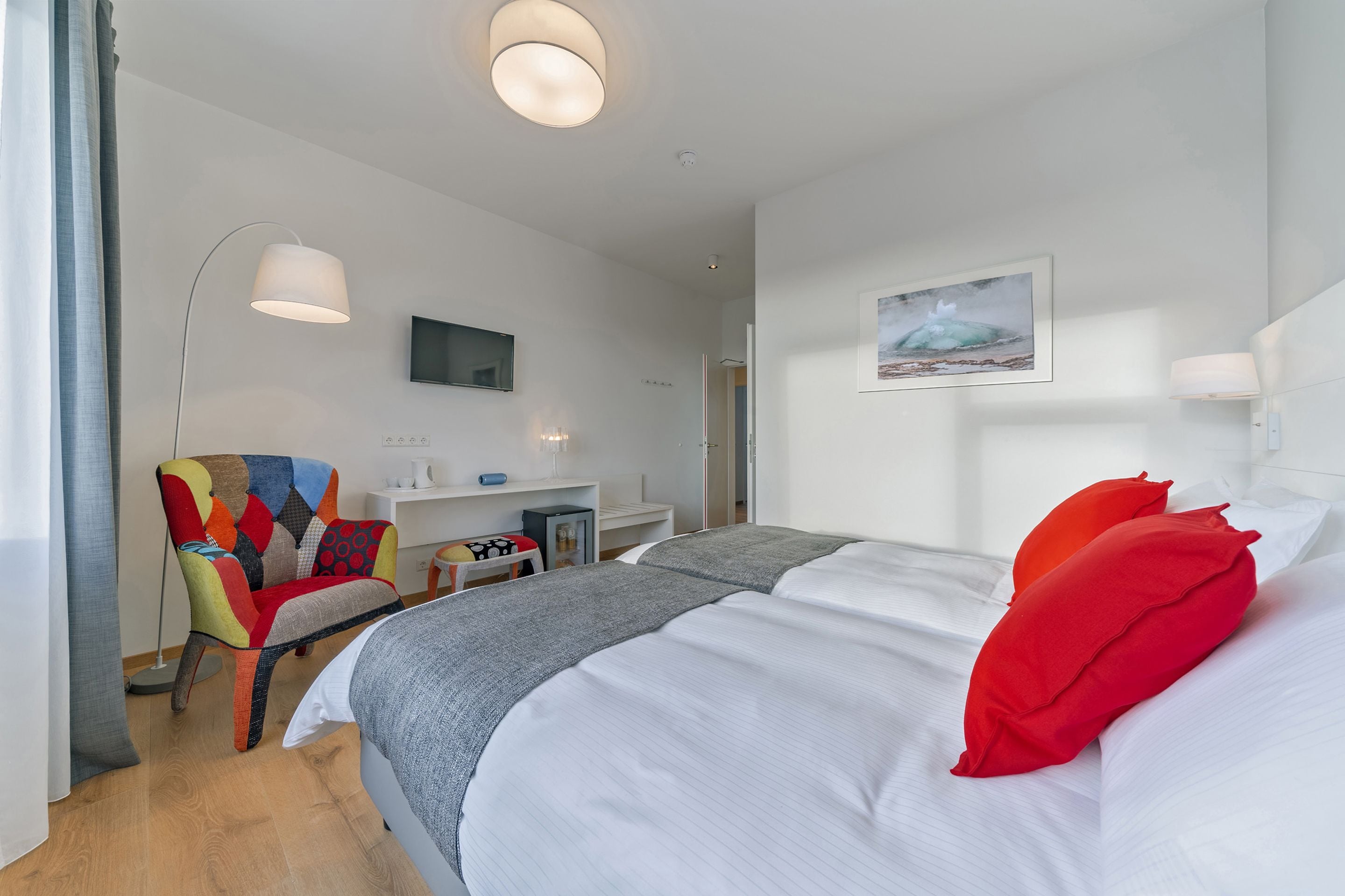 Una habitación de hotel con una cama grande, un sillón colorido, un escritorio con una computadora y un cuadro en la pared.