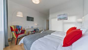 Una habitación de hotel con una cama grande, un sillón colorido, un escritorio con una computadora y un cuadro en la pared.