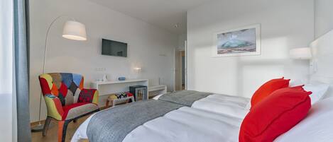 Een hotelkamer met een groot bed, een kleurrijke fauteuil, een bureau met een computer, en een schilderij aan de muur.