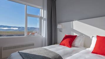 A hotel room with a large window, a bed with white and red bedding, and a view of mountains.