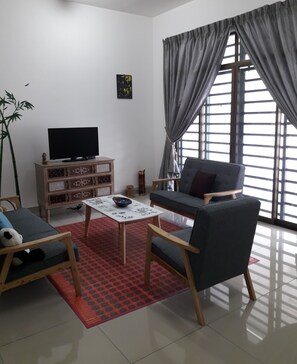 A living room with a sofa, armchair, TV, and a decorative plant. - Tampoi Homestay (Johor Bahru)
