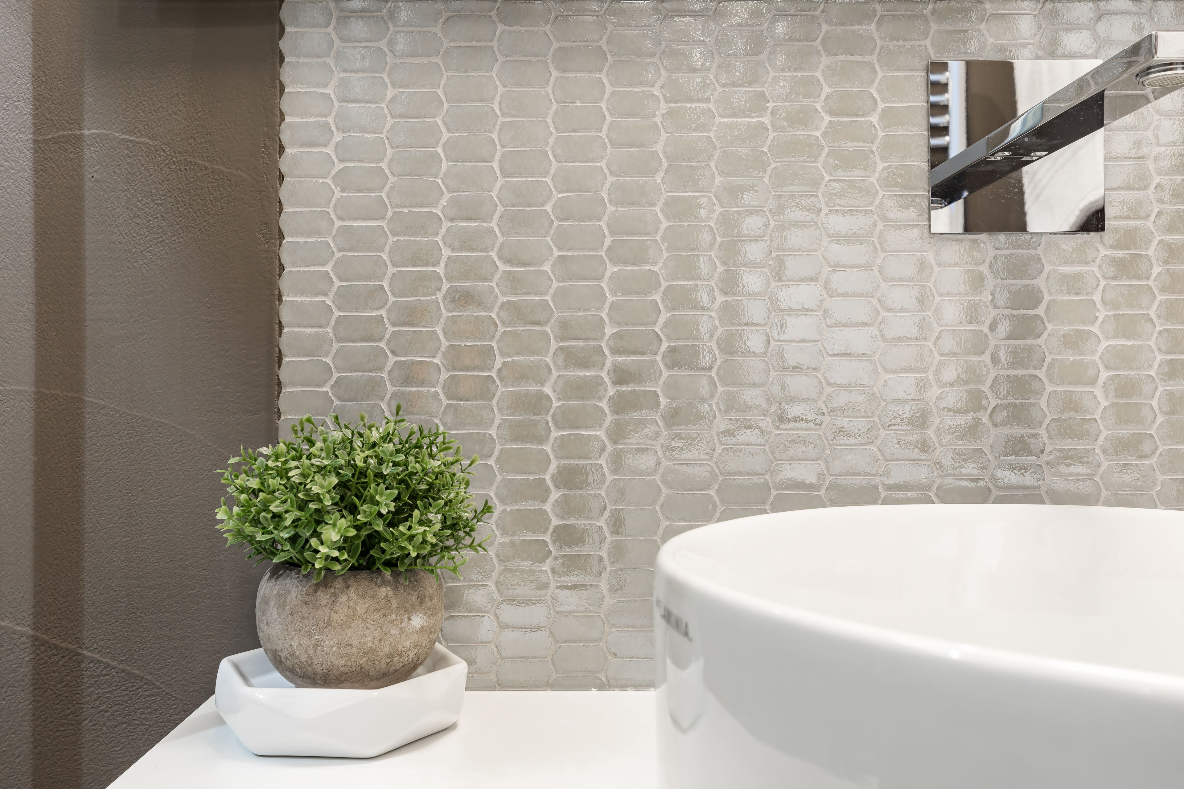 Une salle de bain avec un lavabo blanc, une plante en pot et un mur carrelé.