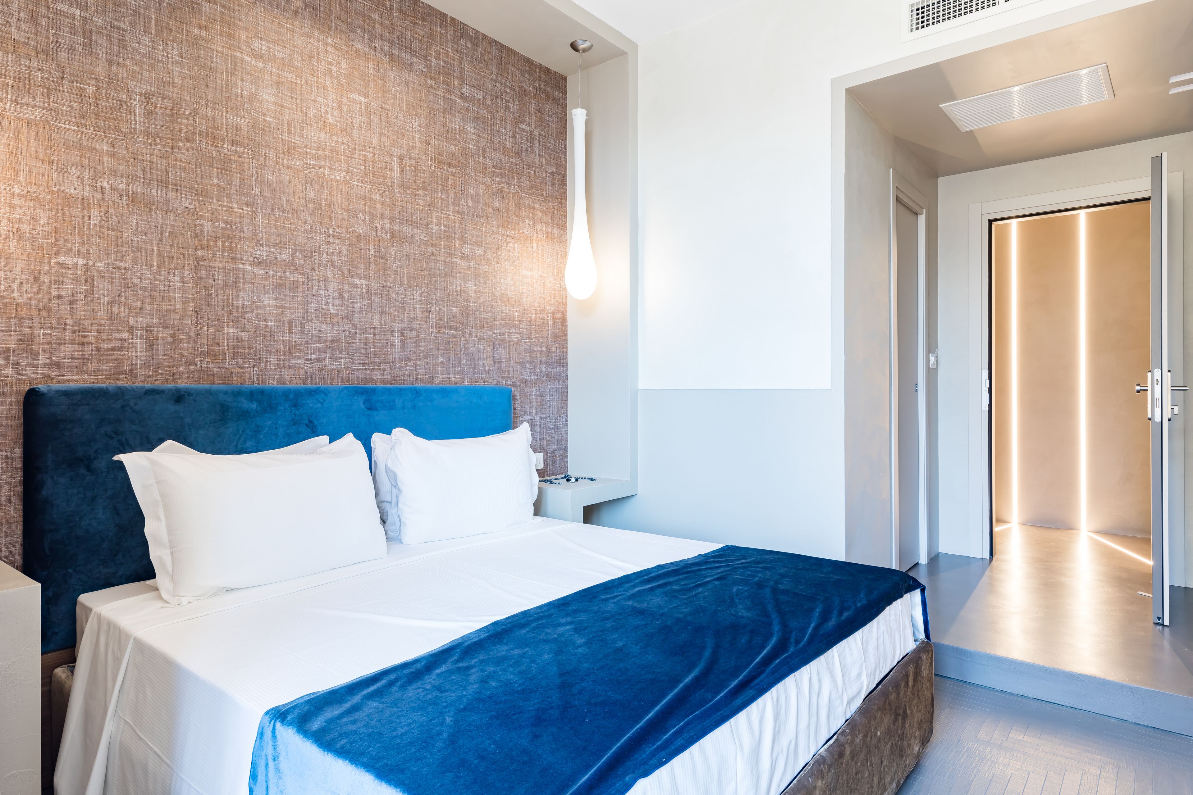 Une chambre d’hôtel moderne avec un grand lit, une tête de lit bleue et un mur d’accent en bois.