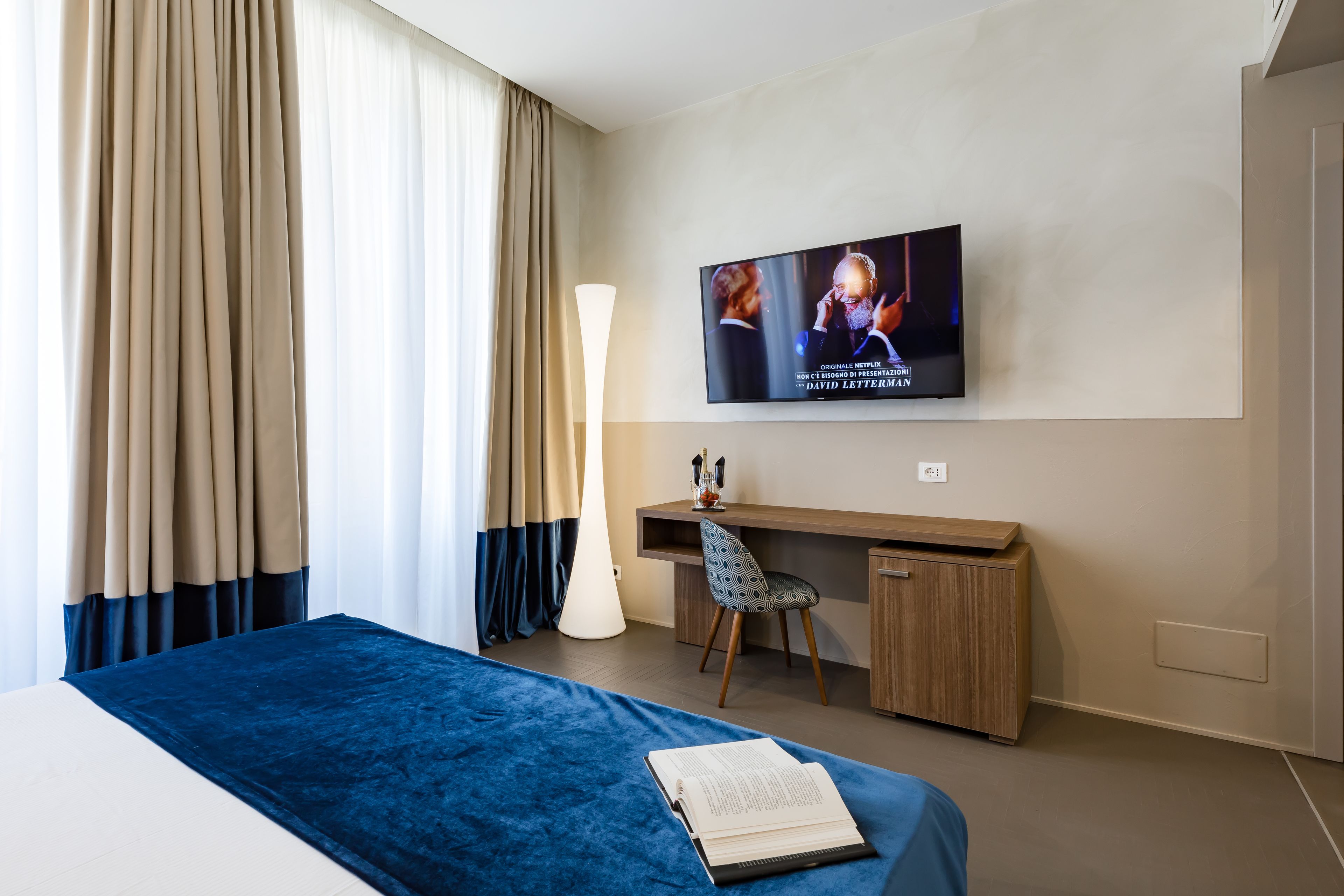 Una habitación de hotel con cama, escritorio, silla, televisión y cortinas.