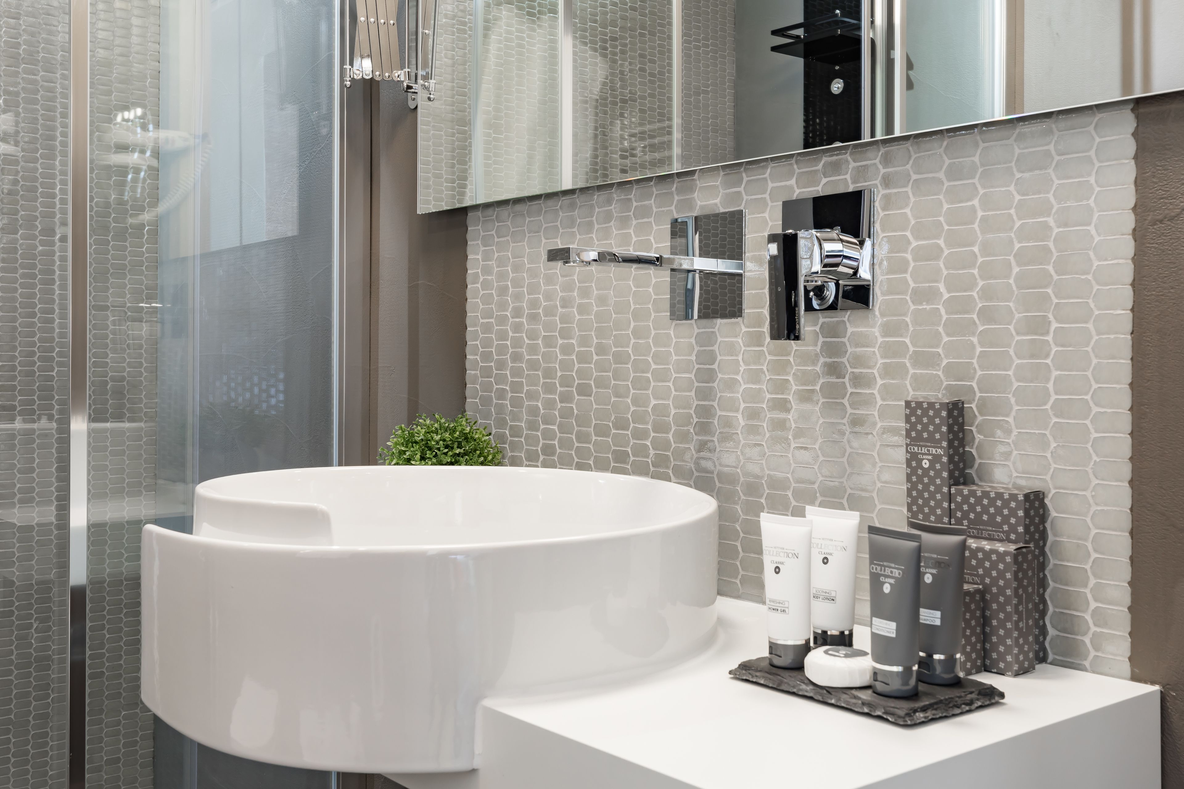 Un baño moderno con un lavabo grande de color blanco, cabina de ducha con paredes de cristal y un salpicadero de azulejos.