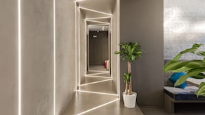 Un couloir moderne agrémenté de luminaires aux formes géométriques, d’une plante en pot et d’un coin salon avec des coussins.
