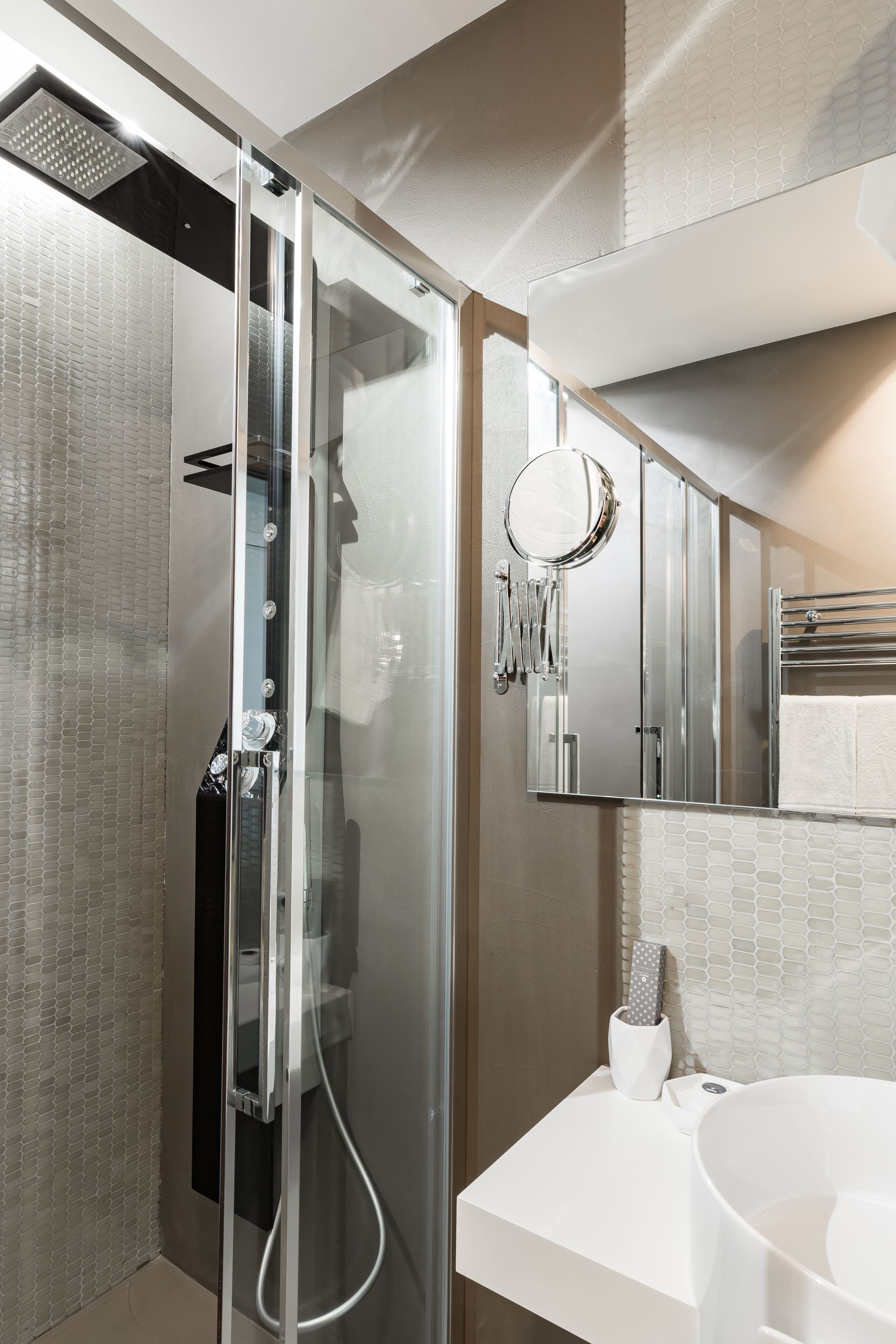 A modern bathroom with a glass-enclosed shower, a white sink, and a mirror above the sink.