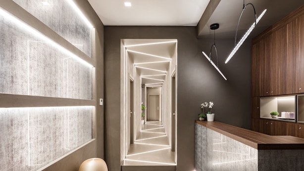 Un intérieur moderne avec un couloir menant à une cuisine, agrémenté d’un éclairage original installé sur les murs et le plafond.