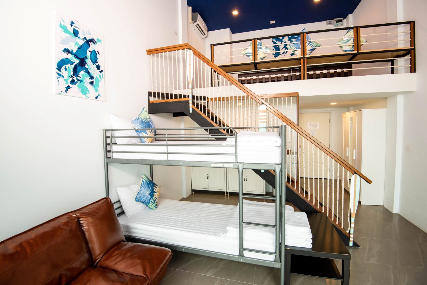 Una cama nido con escalera de madera y pared blanca con un cuadro abstracto azul.
