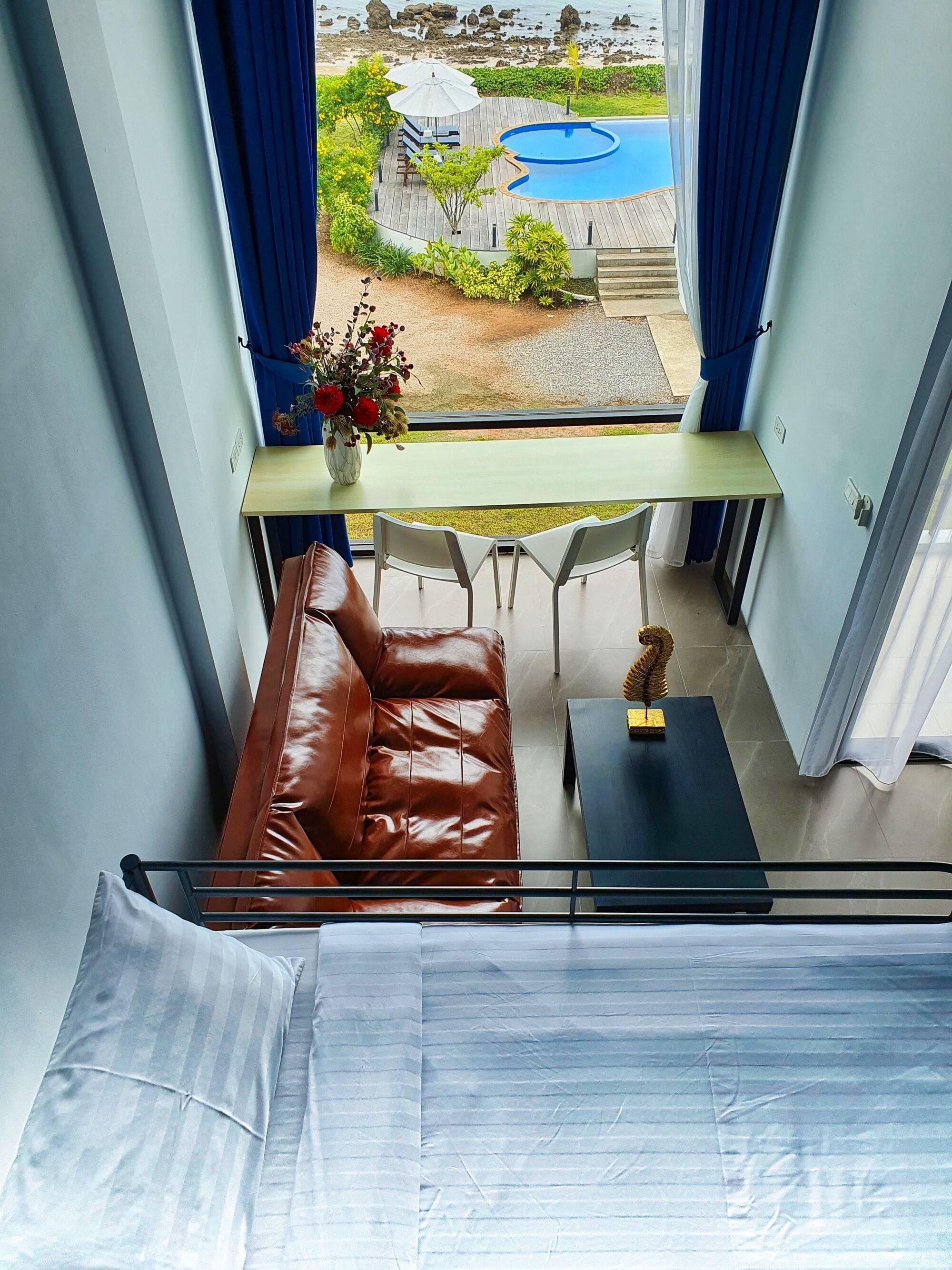 A balcony with a view of a swimming pool, a brown leather sofa, a small table, and a vase of flowers.