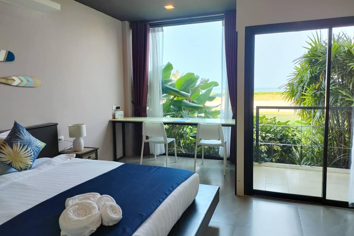 A hotel room with a bed, a desk, and a balcony with a view of the beach.