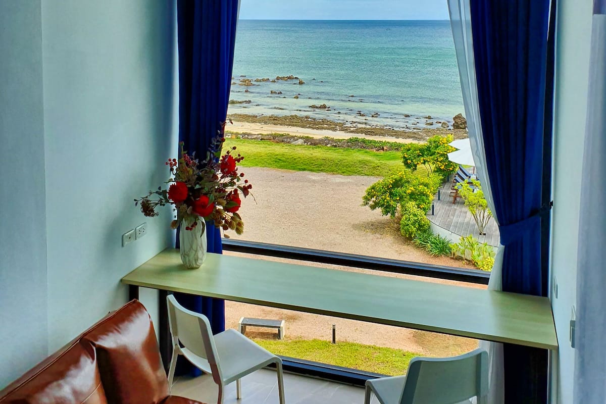 A room with a view of the sea, a brown leather sofa, and a table with chairs.